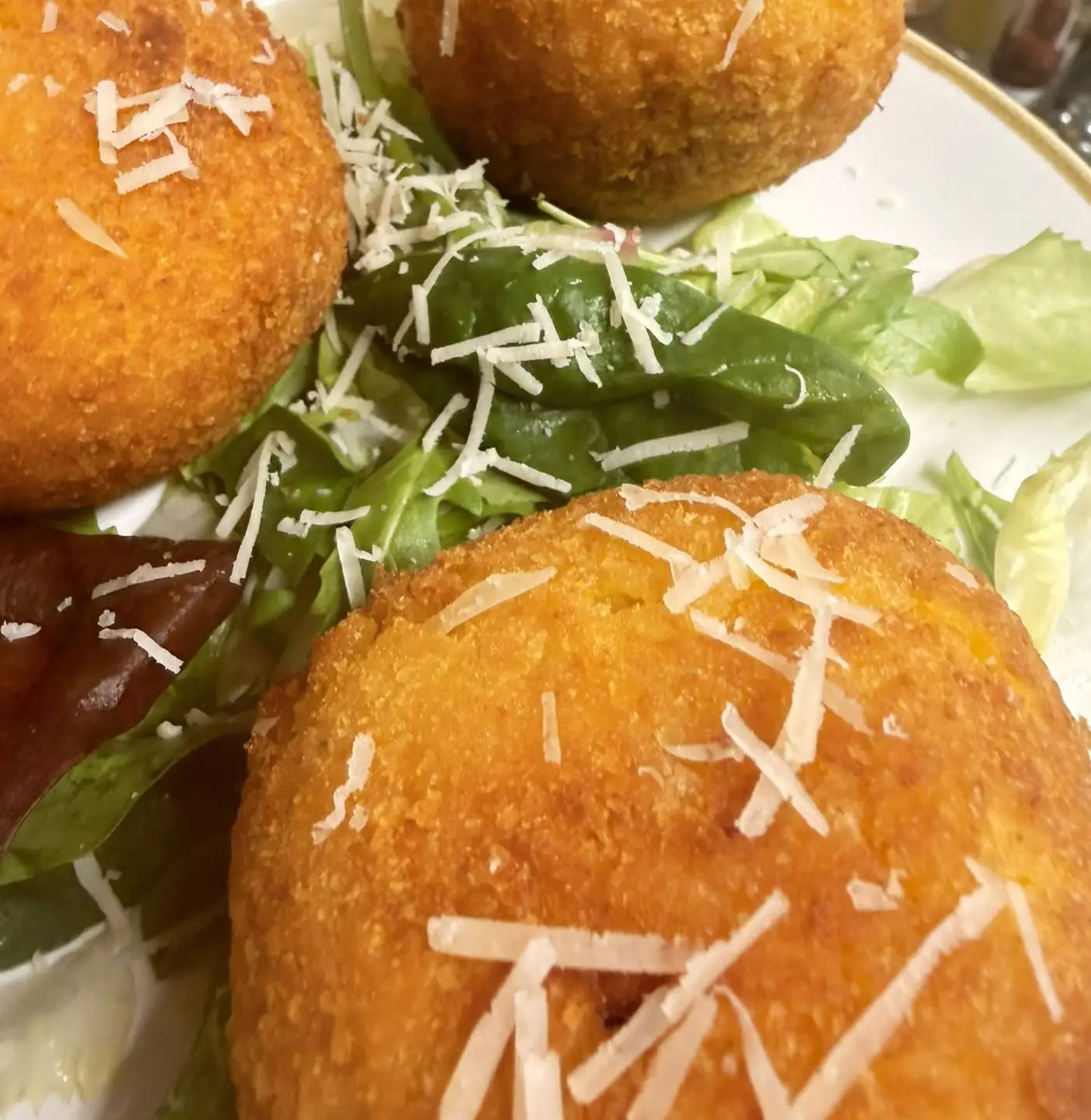 Three golden arancini with parmesan on mixed leaves