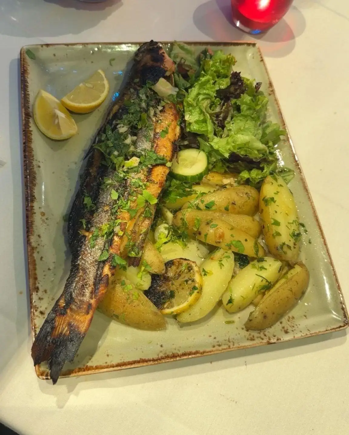 Whole grilled sea bass with salsa verde, lemon and new potatoes on a green platter