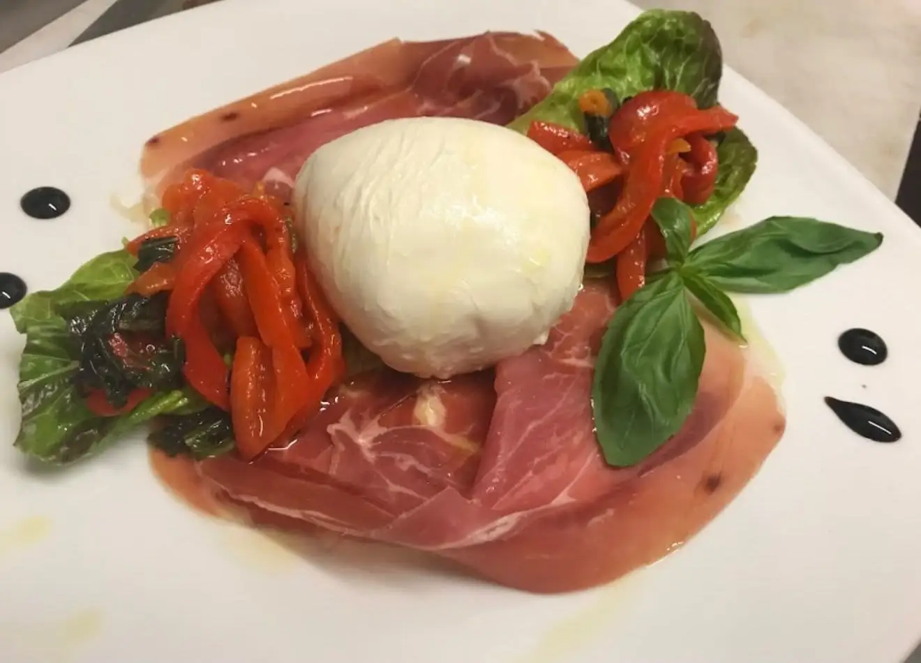 A ball of burrata on slices of prosciutto with roasted red peppers and basil