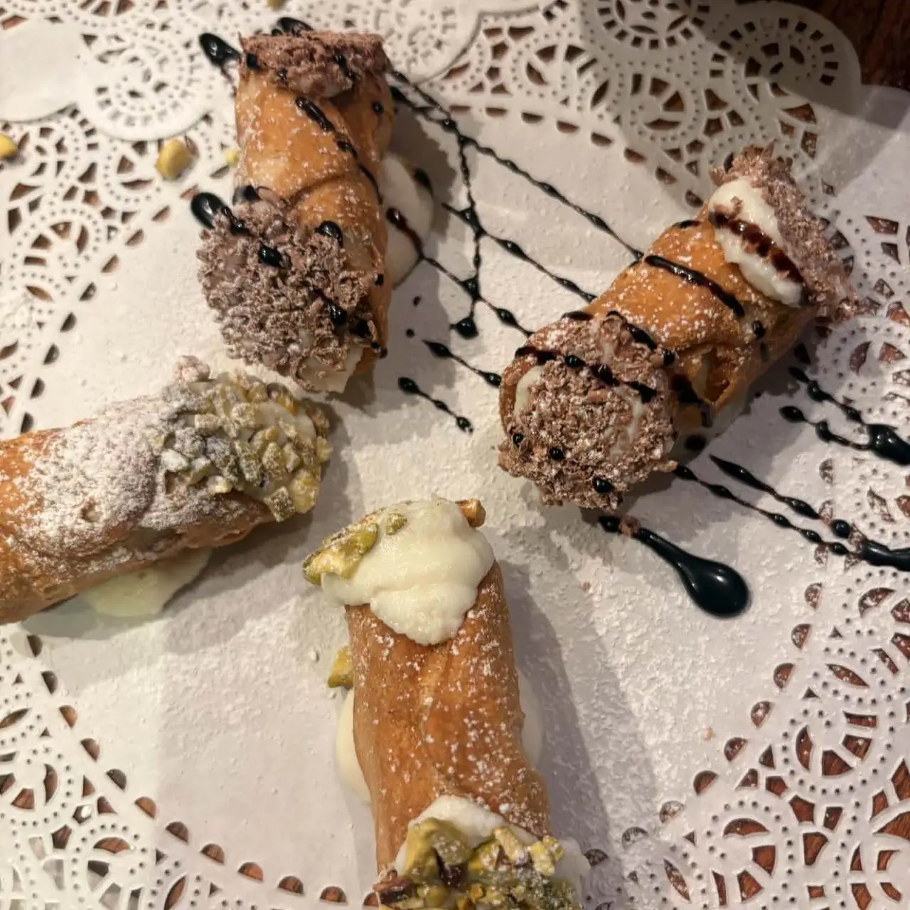 Four cannoli on a lace doily, two with pistachio ends and two with chocolate
