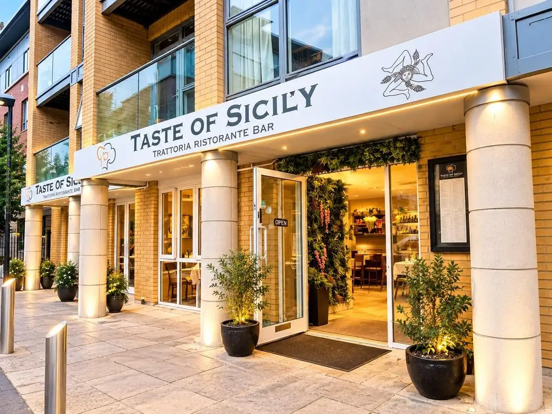 The Taste of Sicily shopfront lit up at dusk, door open