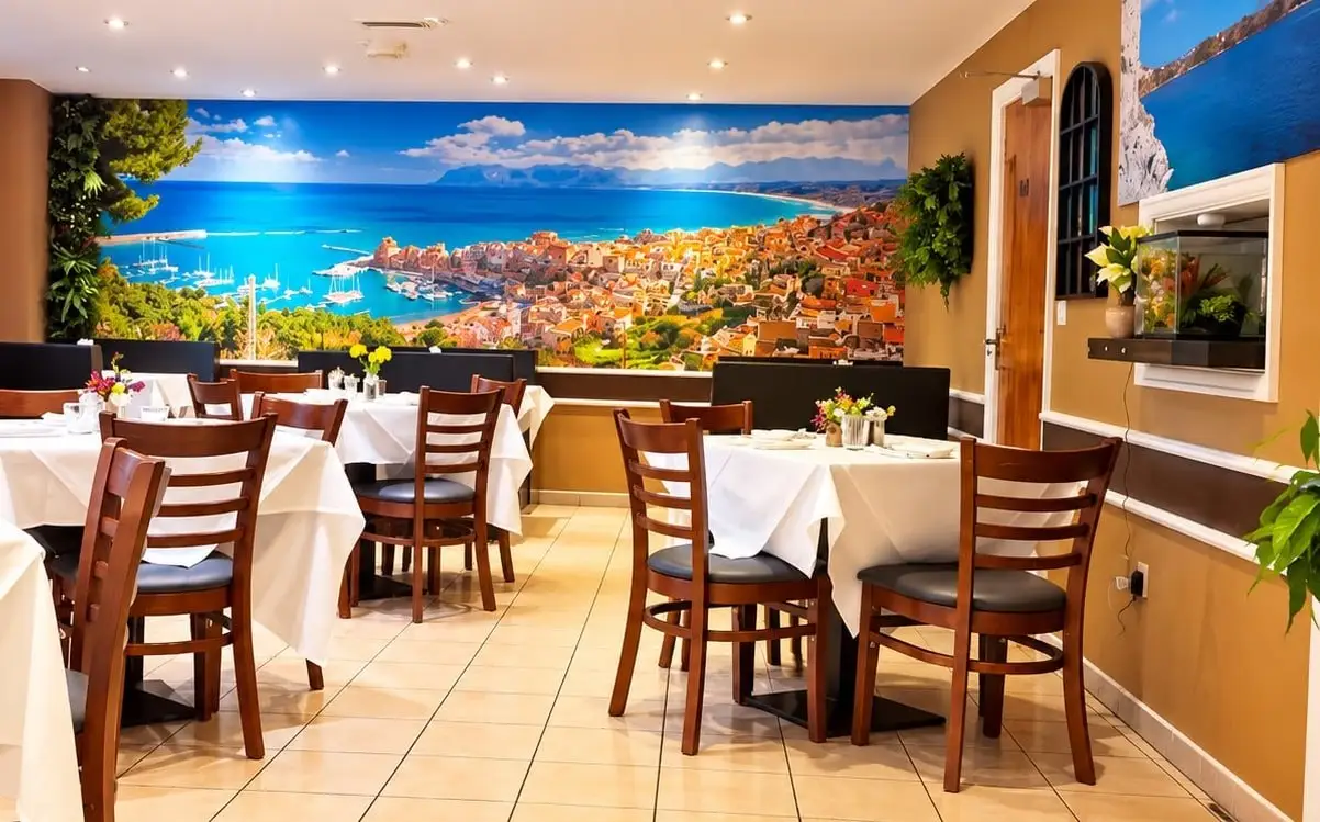 Dining room with white tablecloths in front of a wall-wide mural of a Sicilian harbour town