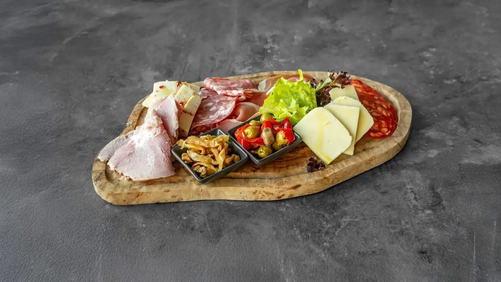 Olive-wood board of cured meats, cheeses, olives and pickled peppers