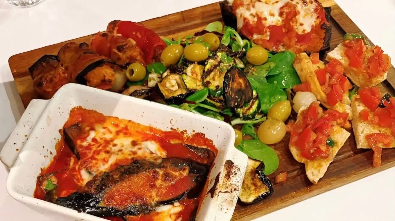 Board of Sicilian vegetable antipasti beside a dish of aubergine parmigiana
