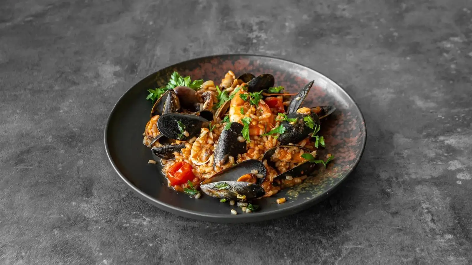 Seafood risotto with mussels, king prawn and baby squid on a dark speckled plate