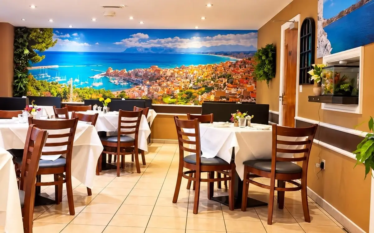The dining room, white tablecloths and dark wood chairs in front of a wall-wide mural of a Sicilian harbour